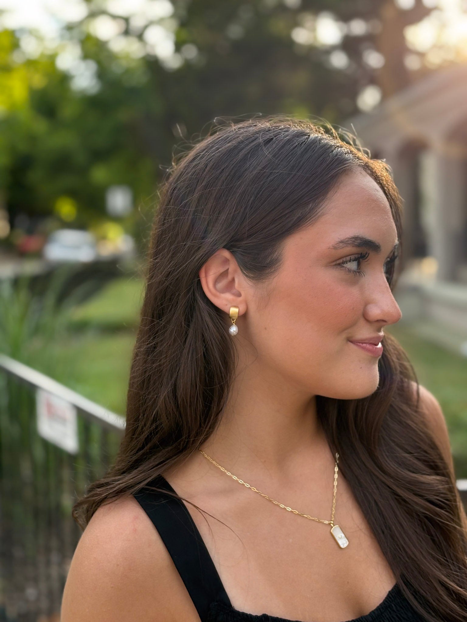 Female wearing gold and pearl earrings and gold necklace with mother of pearl pendant