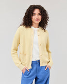 Person wearing a light yellow cardigan over a white shirt with blue pants on a plain background